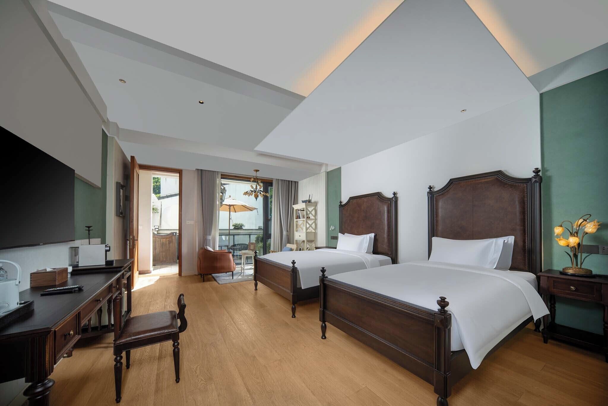 A hotel room with two wooden beds, a desk, a chair, and a TV.