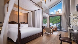 A four-poster canopy bed with a wooden headboard, a chandelier, and a view of a mountainous landscape through large windows. - HeartLand Logde MoGanShan. (Huzhou)