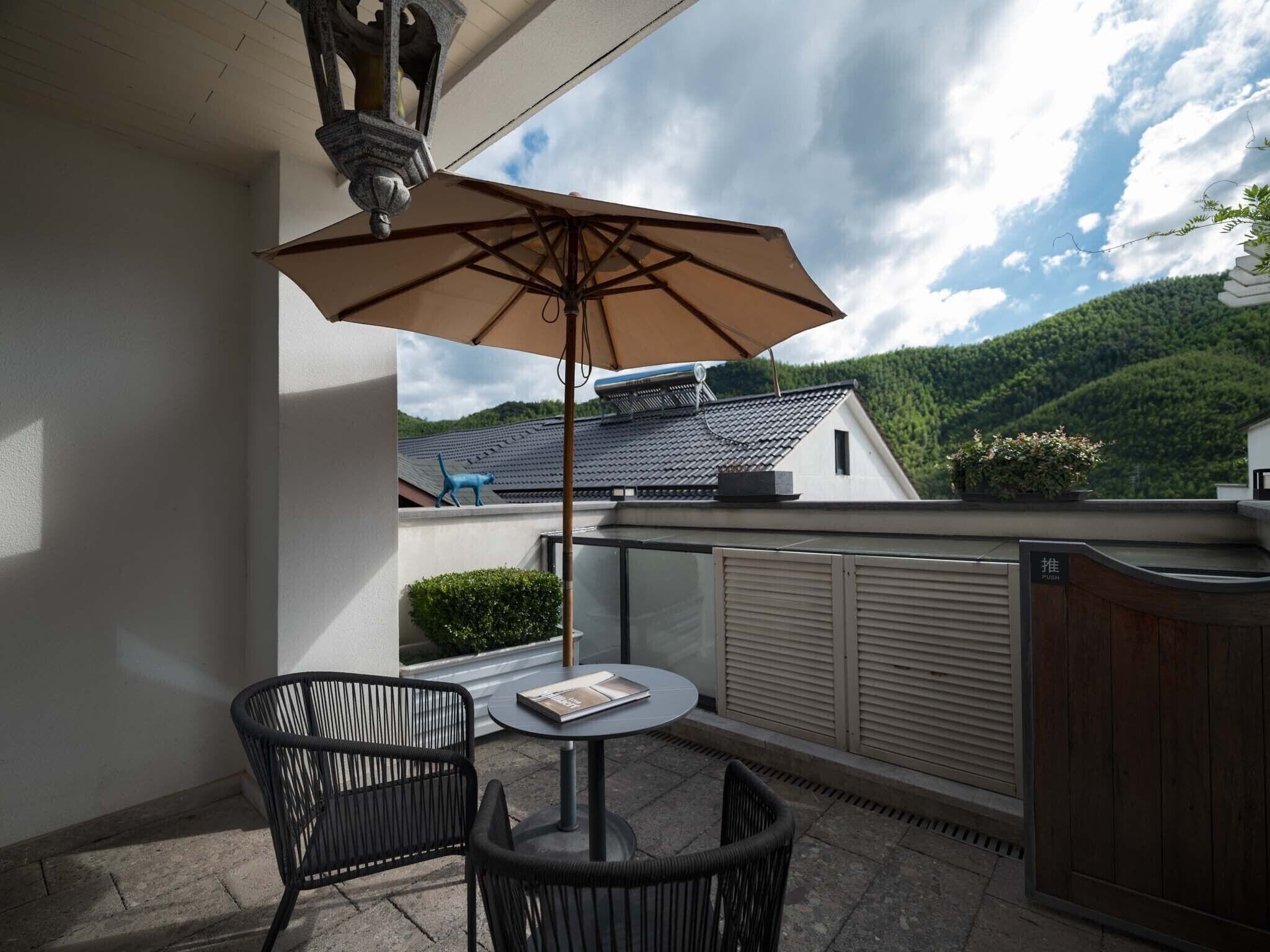 Ein Balkon mit Tisch und Stühlen, einem großen Sonnenschirm und Blick auf einen Berg.