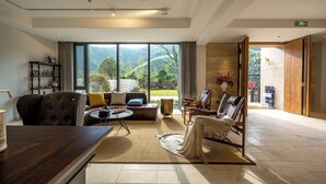 A spacious living area with a large window offering a view of a mountainous landscape. There is a leather sofa, a coffee table, and a seating area with a woven rug. - HeartLand Logde MoGanShan. (Huzhou)