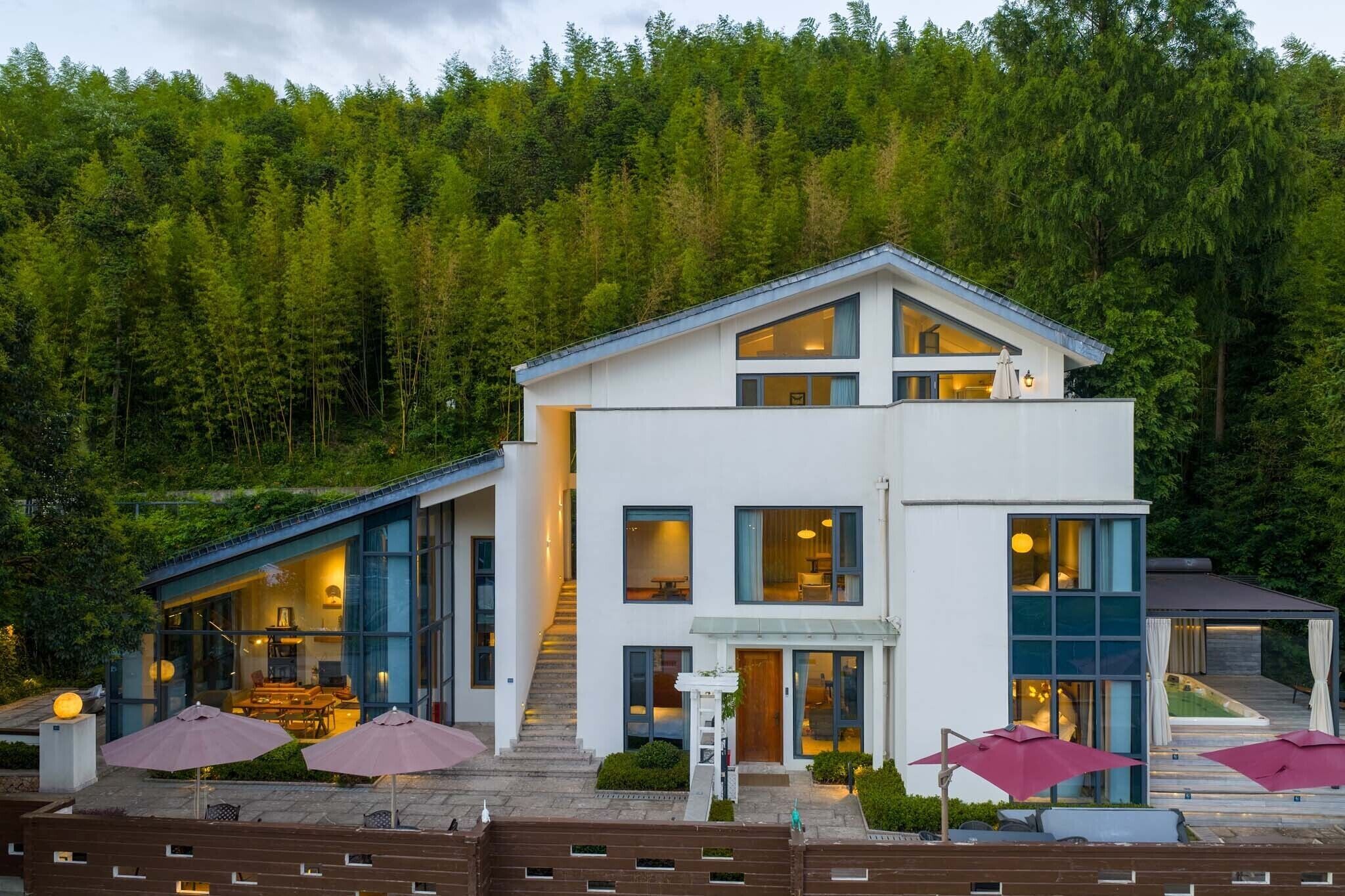 Ein modernes, zweistöckiges Gebäude mit großen Fenstern, einer überdachten Außenbereich-Sitzgelegenheit und einer Treppe, die zum oberen Stockwerk führt.