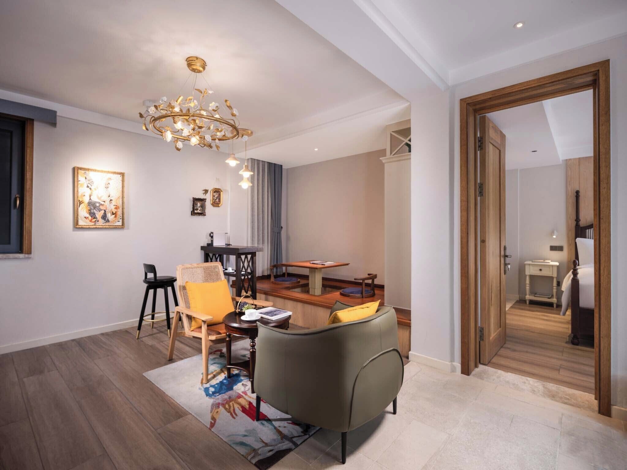 A modern living room with a chandelier, a dining area, and a bedroom visible through an open door.