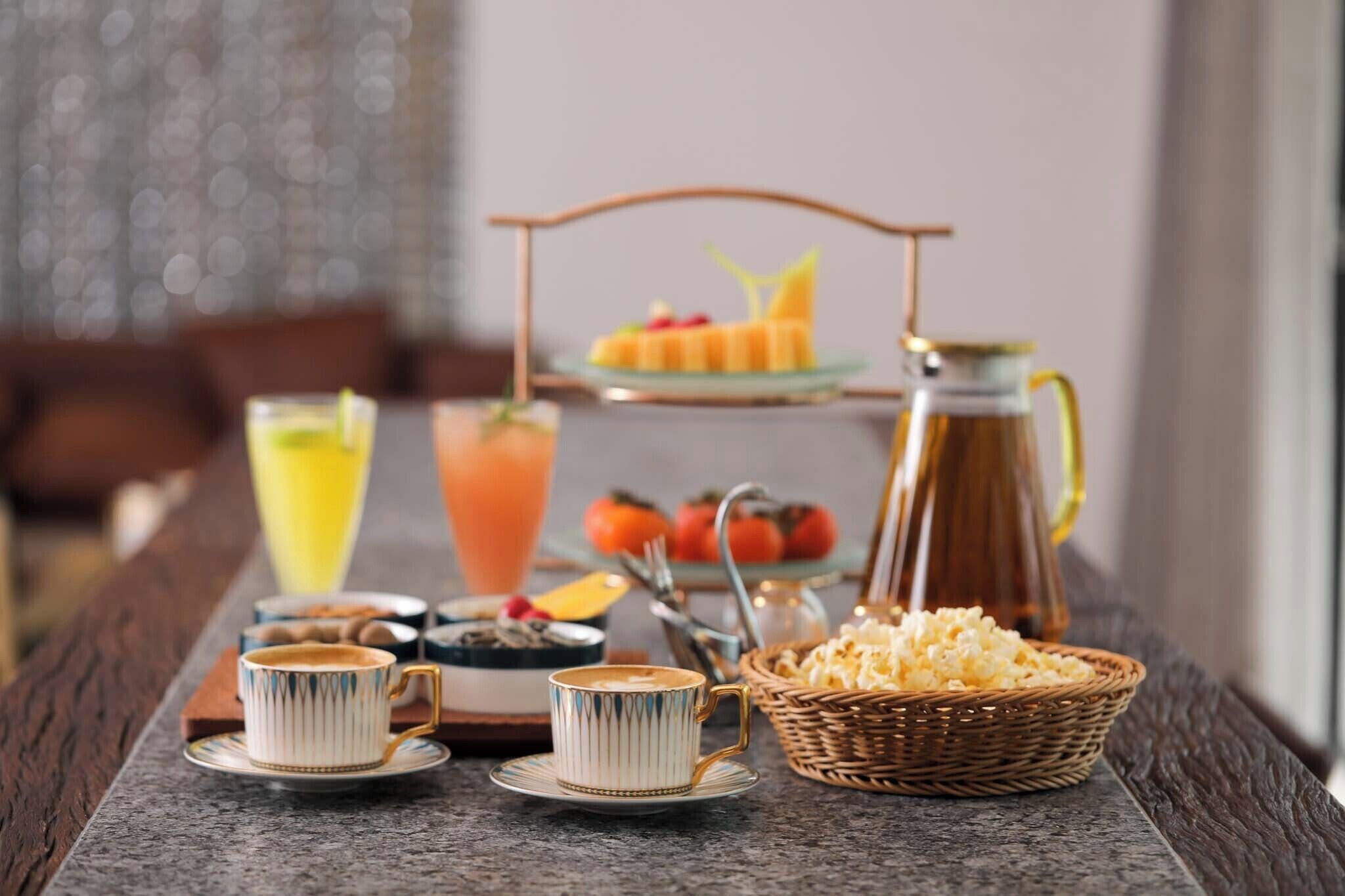 Desayuno con taza de café, vaso de jugo de naranja, jarra y presentación de frutas.