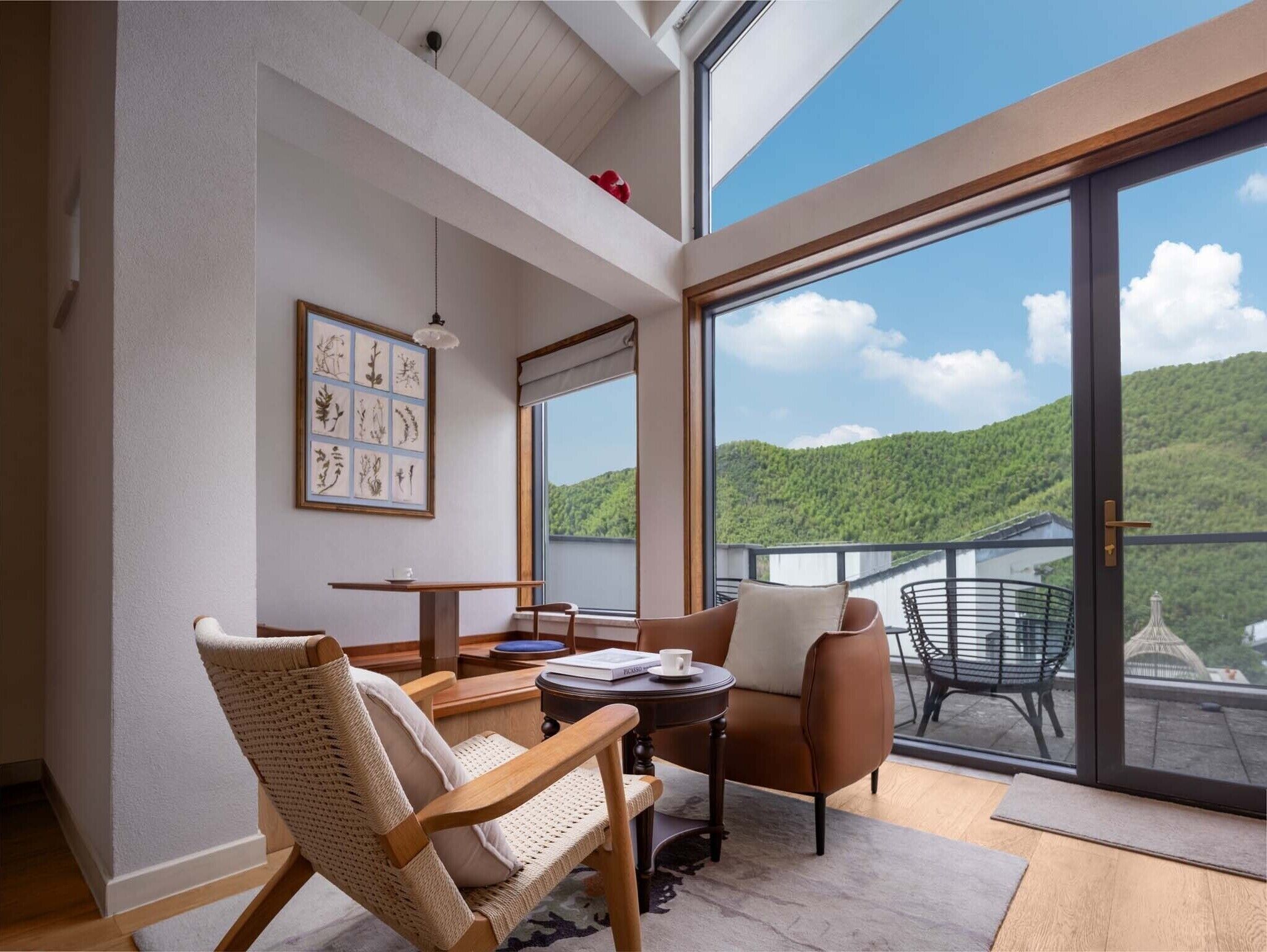 Una habitación moderna con un amplio ventanal corredero que da a un balcón con vistas panorámicas a colinas verdes.