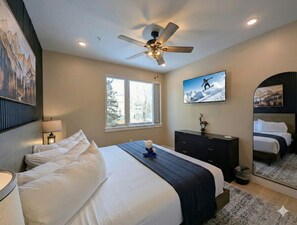 A bedroom with a large bed, a ceiling fan, a TV, a dresser, and a window with a view of trees. - New Luxury | Keystone Lake | King Bed (Keystone)