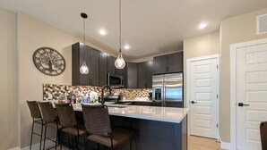 A modern kitchen with dark cabinets, a stainless steel refrigerator, a microwave, and a large island with bar stools. - New Luxury | Keystone Lake | King Bed (Keystone)