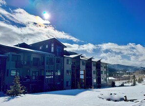 A multi-story building with a snow-covered ground, a clear sky, and mountains in the background. - New Luxury | Keystone Lake | King Bed (Keystone)