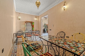 Zona pranzo con tavolo e sedie decorati, soffitto ornamentale e vista su un'altra stanza.