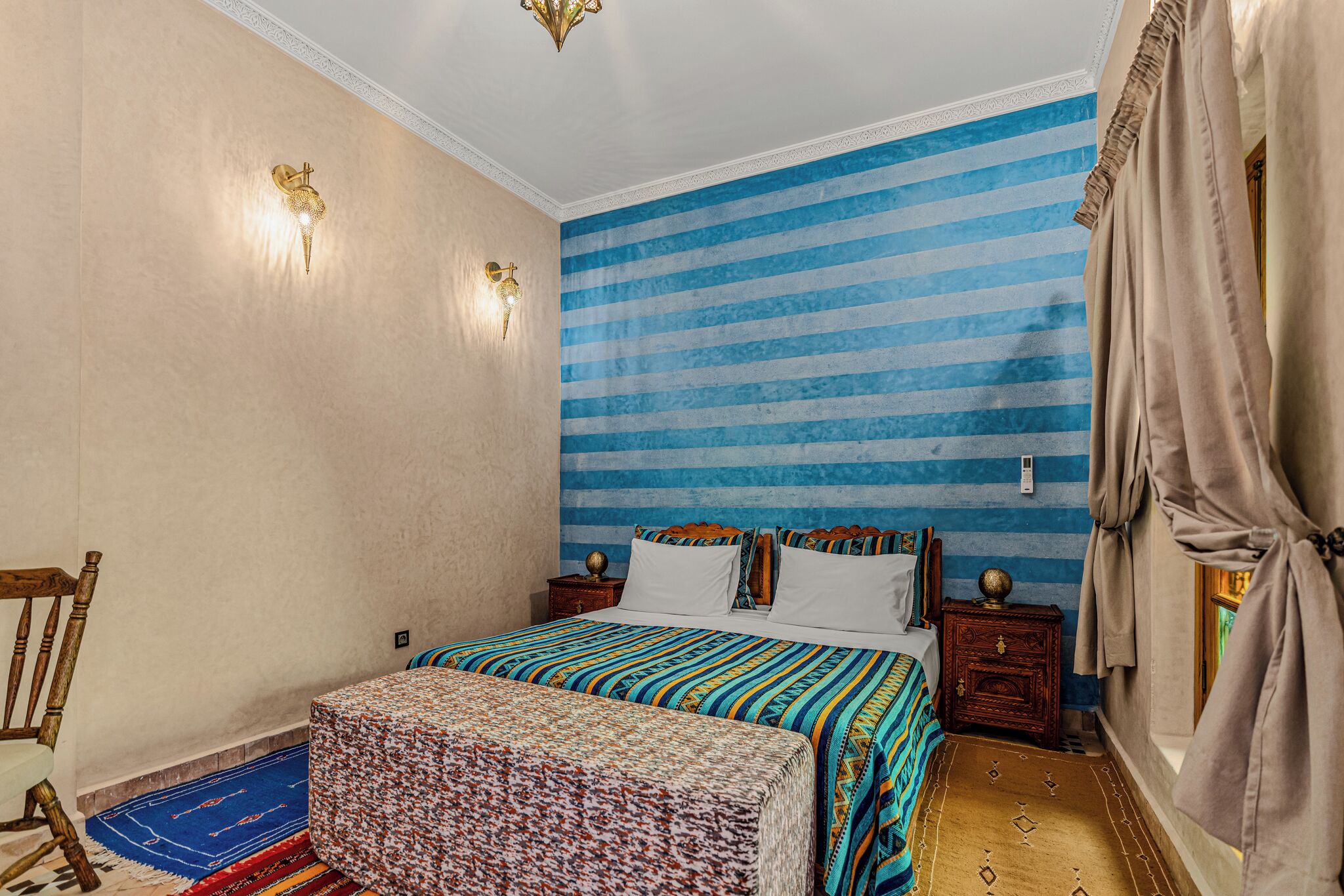 A bedroom with a bed, two bedside tables, a chair, a rug, and a curtain.