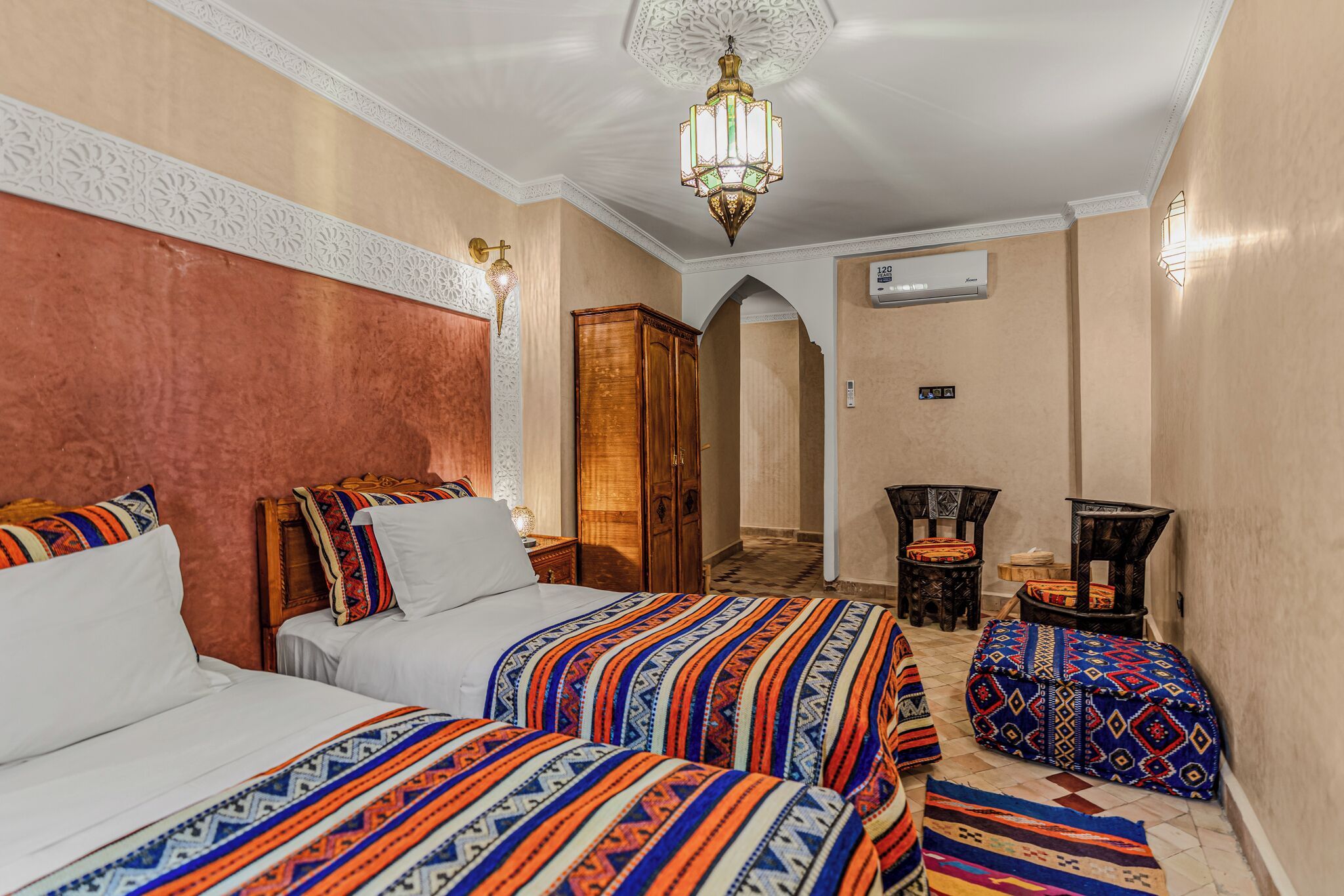 Une chambre d’hôtel avec deux lits, un lustre, une armoire et une petite table avec une lampe.