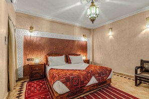 A bedroom with a large bed, a nightstand, a chair, and decorative wall panels. - Riad Maison D'HÔTE ABDEL & JAMILA (Marrakech)