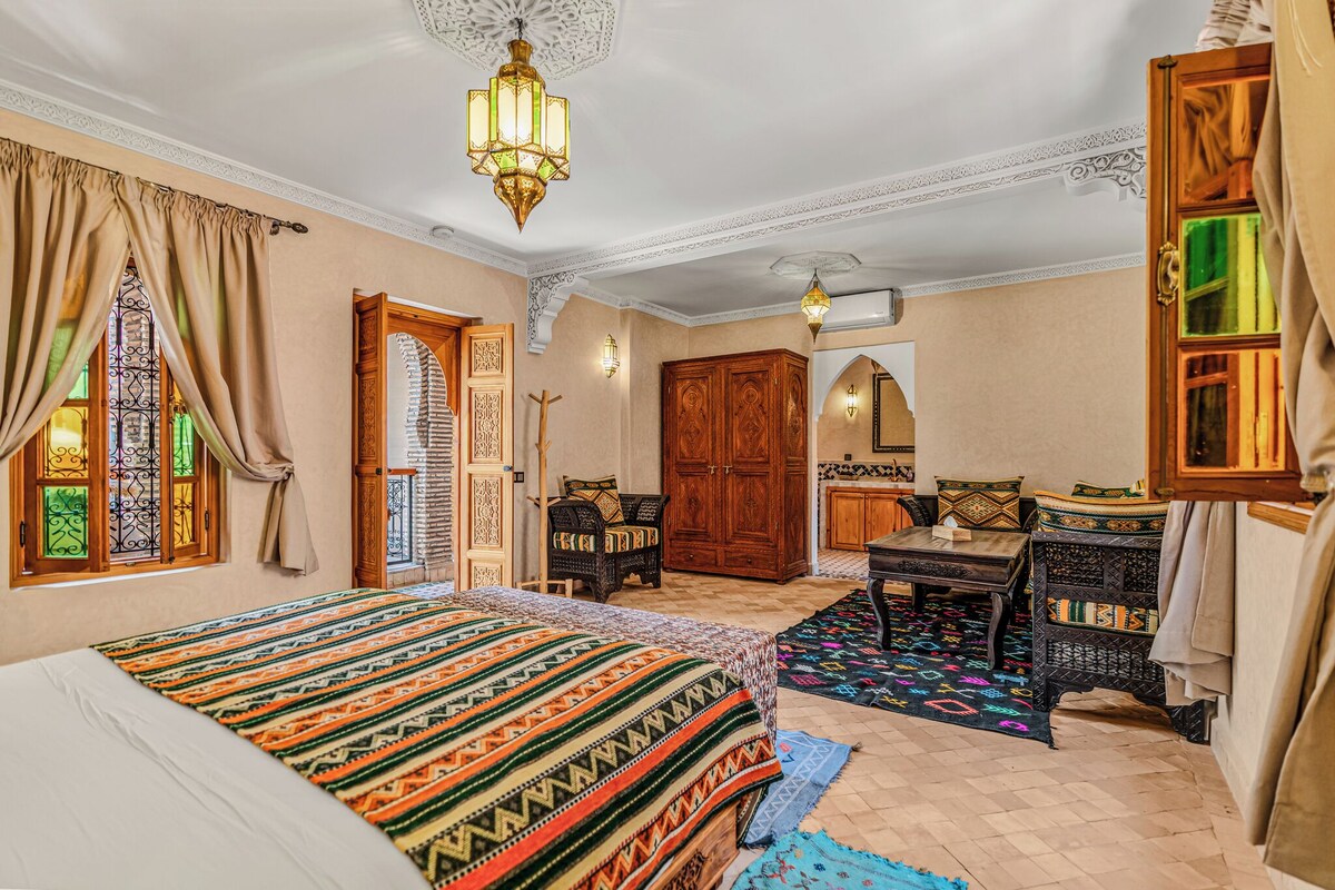 A traditional room with a bed, a wooden wardrobe, a small table, and a decorative lamp.