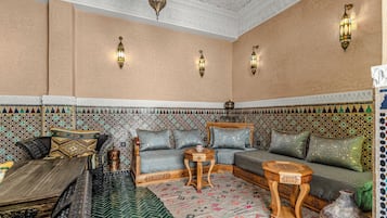A traditional Moroccan interior with a patterned wall, a sofa set, a wooden coffee table, and a decorative lantern.