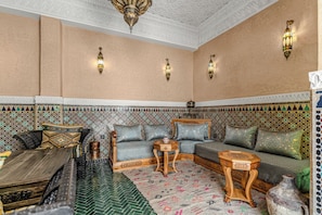 A traditional Moroccan interior with a patterned wall, a sofa set, a wooden coffee table, and a decorative lantern. - Riad Maison D'HÔTE ABDEL & JAMILA (Marrakech)