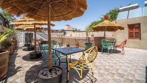 An outdoor patio with thatched umbrellas, metal chairs, and potted plants. - Riad Maison D'HÔTE ABDEL & JAMILA (Marrakech)
