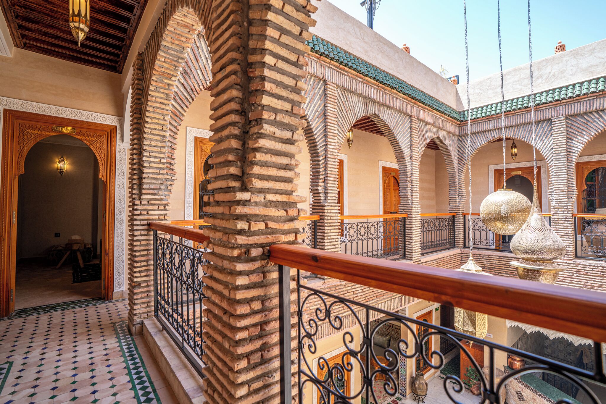 Un interior tradicional marroquí con piso de azulejos, puertas de madera ornamentadas y un balcón con barandilla de hierro forjado.