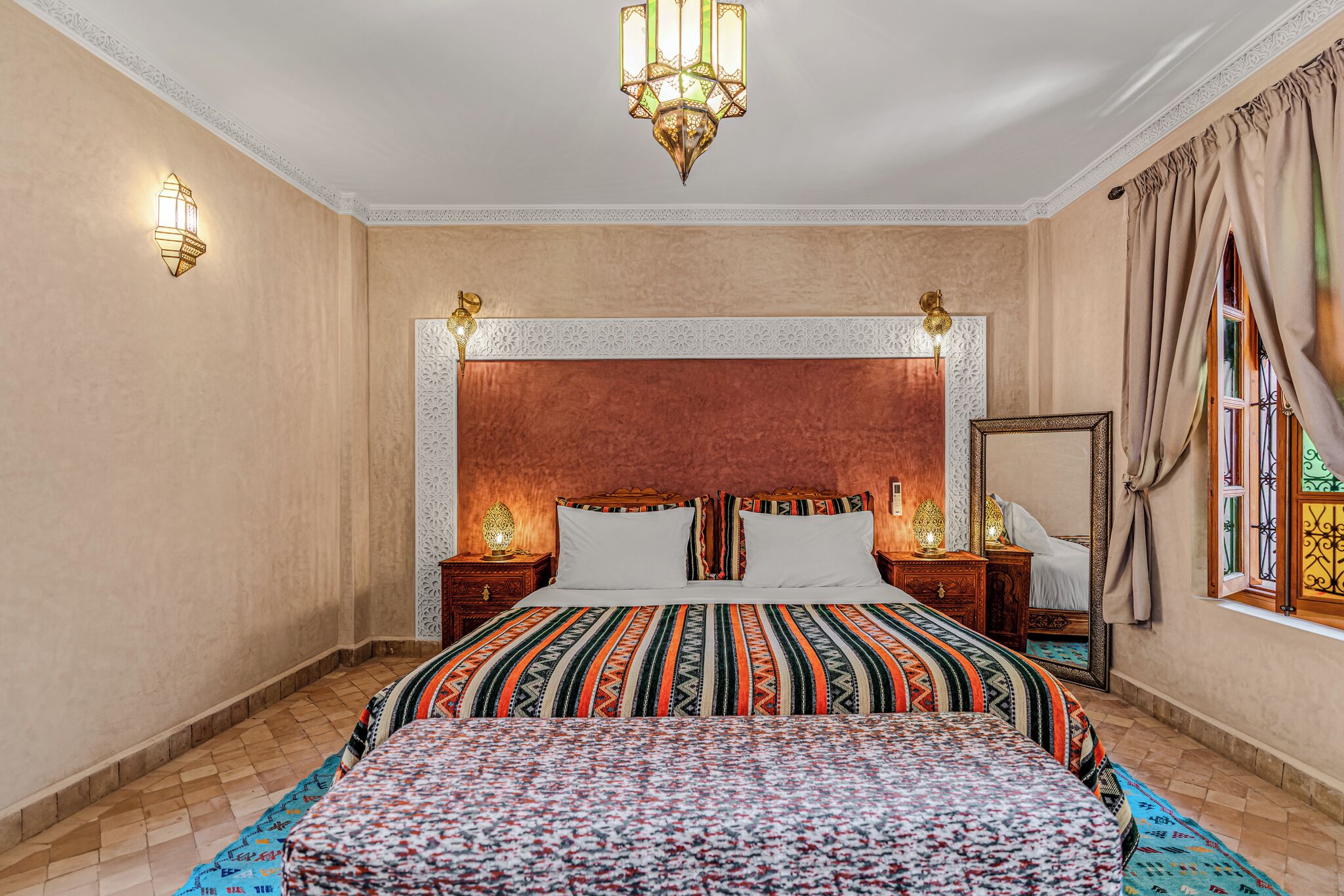 Et hotelværelse med en stor seng, to sengeborde, et natbord, et spejl og en dekorativ loftlampe.