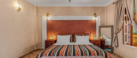 A hotel room with a large bed, two bedside tables, a nightstand, a mirror, and a decorative ceiling light.