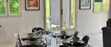 A dining area with a table set for six, large windows, and framed artwork on the walls.