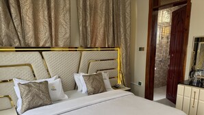 A hotel room with a large bed, a bedside table, a mirror, and a wardrobe. - Pera Imperial hotel (Iringa)