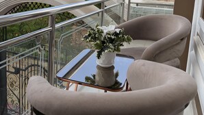 A balcony with a white railing, a potted plant, and two beige armchairs. - Pera Imperial hotel (Iringa)
