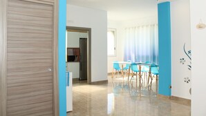 A modern interior with a wooden door, a dining area with blue chairs, and a kitchen visible through an open doorway. - Luca's House (Giovinazzo)