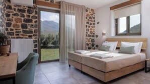 A bedroom with a stone wall, a bed with pillows, a desk, and a view of the outdoors.