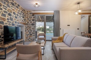 Una sala de estar con paredes de piedra, un televisor de pantalla plana, un sofá, una silla y una mesa con una computadora portátil.