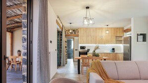 A modern kitchen with wooden cabinets, a dining area with a table and chairs, and a living room with a sofa and a throw blanket.