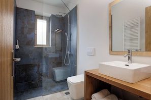 Un baño moderno con ducha envuelta en vidrio, un lavamanos blanco y un tocador de madera.