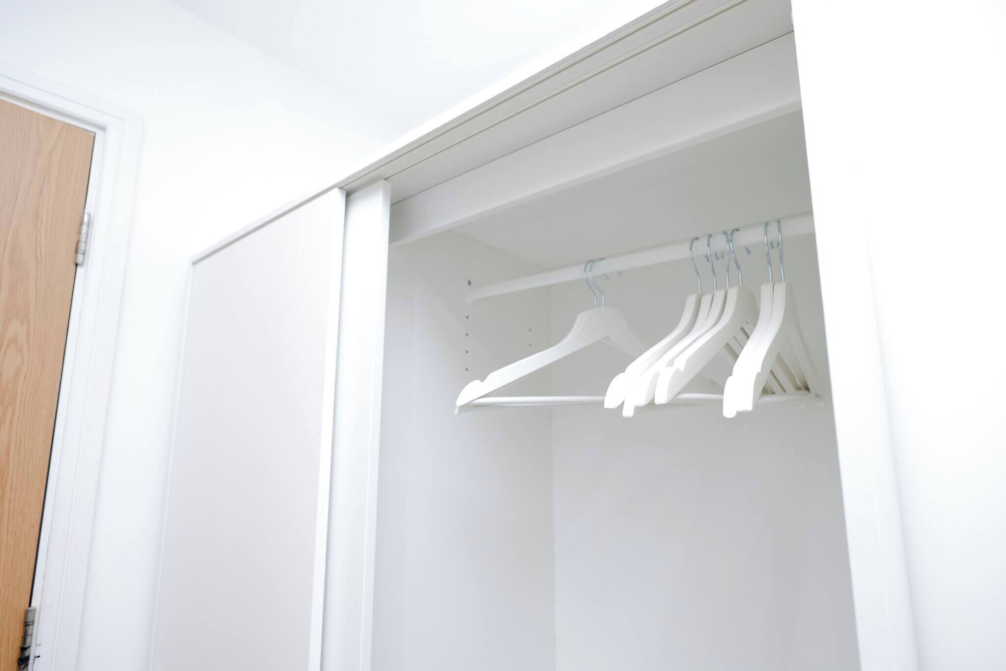A white closet with a wooden door and a white hanger rod.
