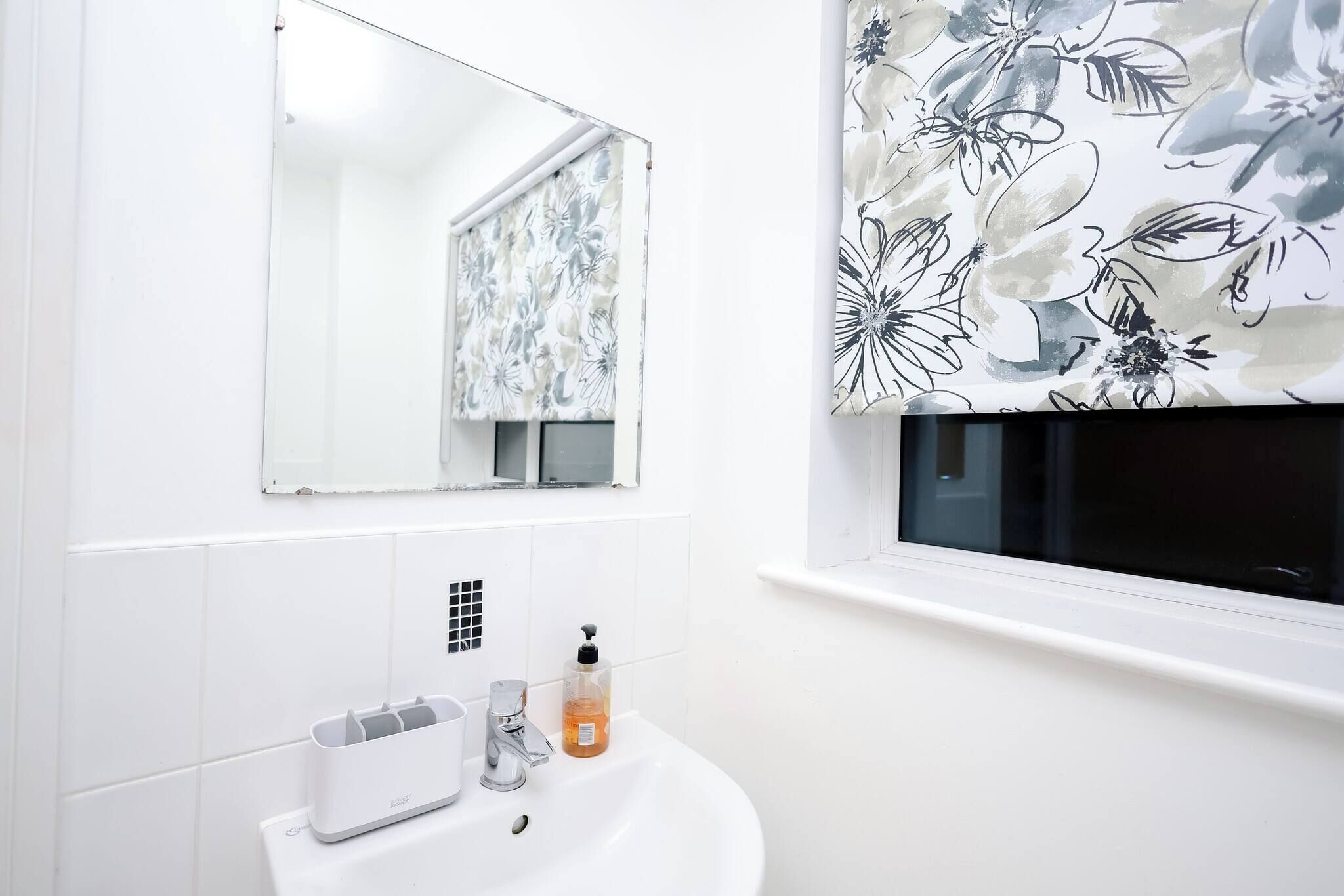 A bathroom with a white sink, a mirror, a window, and a floral wallpaper.