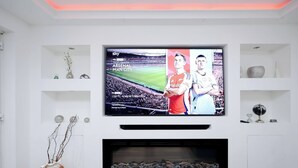 A modern living room with a flat-screen TV mounted on the wall, a fireplace below, and decorative items on shelves. - Cozy Place in Salford, Sleeps 8, 4 Bedroom, 5 Beds (Salford)