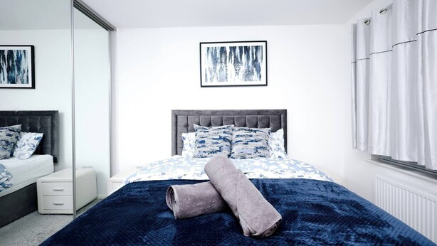 A bedroom with a bed, a bedside table, a mirror, and a window with curtains. - Cozy Place in Salford, Sleeps 8, 4 Bedroom, 5 Beds (Salford)