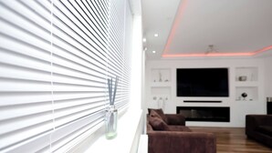 A modern living room with a large flat-screen TV, a brown sofa, and a white radiator. - Cozy Place in Salford, Sleeps 8, 4 Bedroom, 5 Beds (Salford)