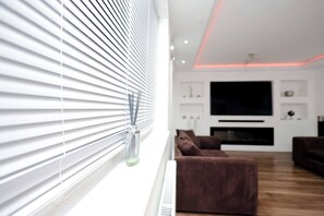 A modern living room with a large flat-screen TV, a brown sofa, and a white radiator. - Cozy Place in Salford, Sleeps 8, 4 Bedroom, 5 Beds (Salford)