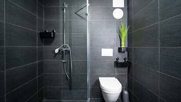 Et moderne badeværelse med mørke fliser, en bruseniche, toilet og en lille hylde med en plante.