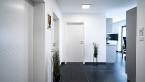 A modern hallway with a white door, a potted plant, and a view into a kitchen area. - Blauer Stein - Echo bl7a-haus (Pulheim)