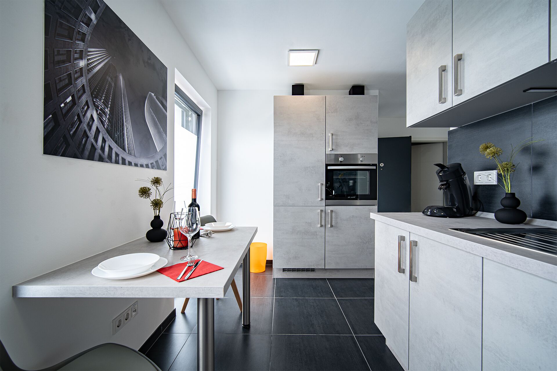 Una cocina moderna con horno empotrado, cafetera y comedor con mesa y sillas.