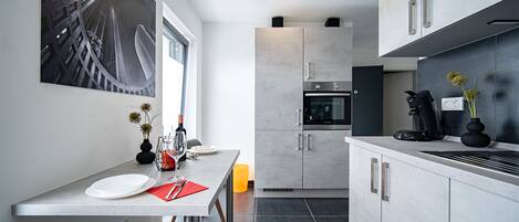 A modern kitchen with a built-in oven, a coffee machine, and a dining area with a table and chairs.