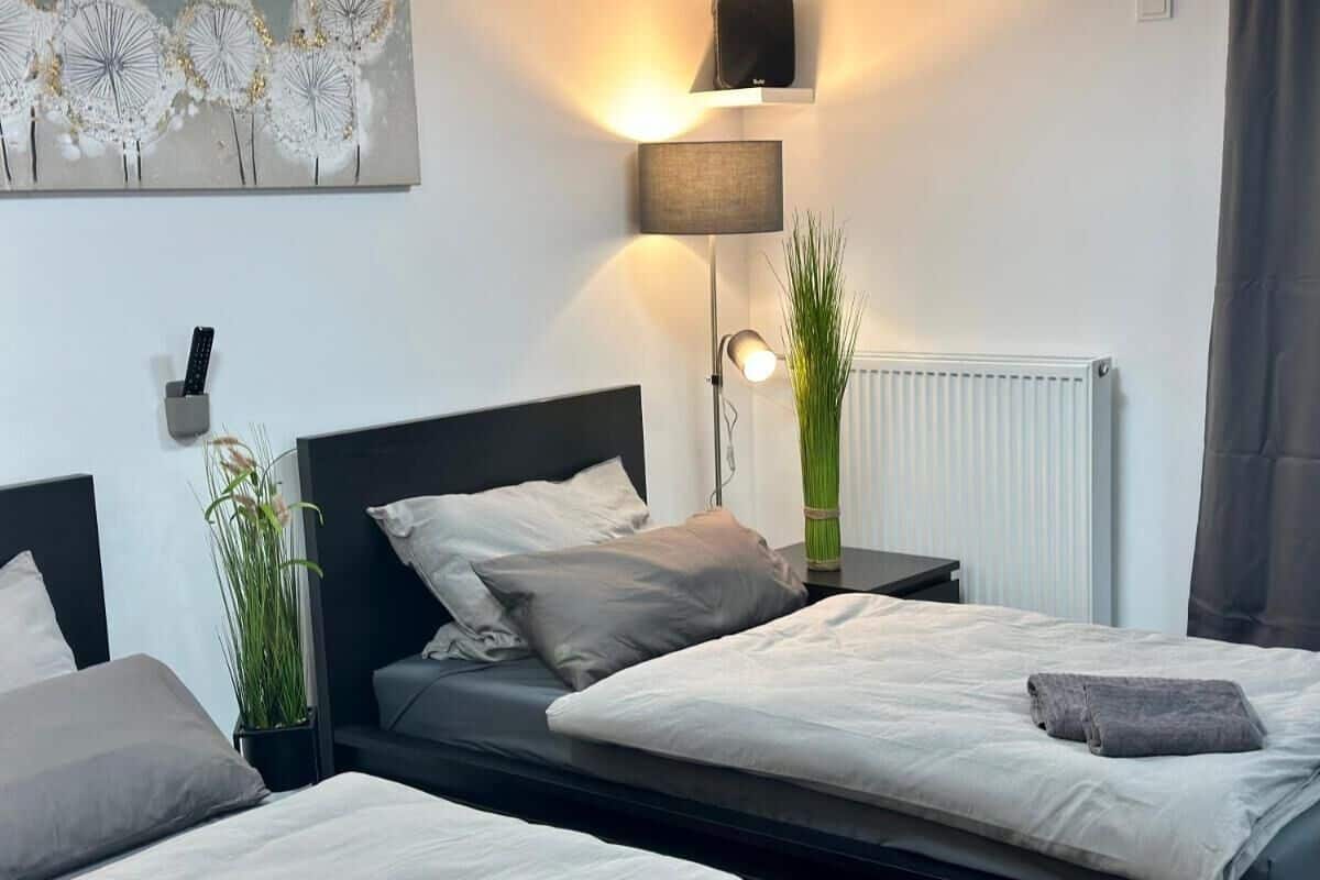 Een moderne slaapkamer met twee bedden, een nachtkastje, een lamp, een radiator en een kunstwerk aan de muur.