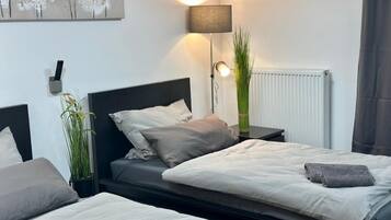 Ett modernt sovrum med två sängar, ett sängbord, en lampa, ett element och en väggdekoration.