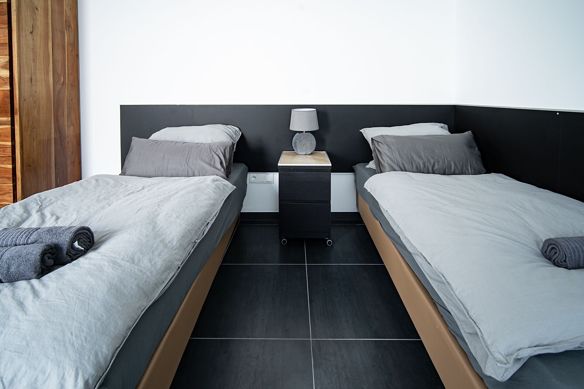 A twin room with two beds, a nightstand, a lamp, and a wooden door.