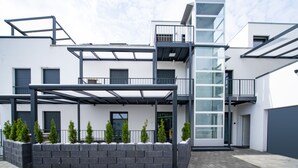 A modern building with a balcony, a glass door entrance, and a brick planter with small trees. - Blauer Stein - Echo bl7a-haus (Pulheim)