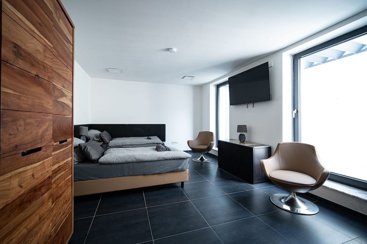 Een moderne slaapkamer met een bed, twee stoelen, een televisie en een groot raam.
