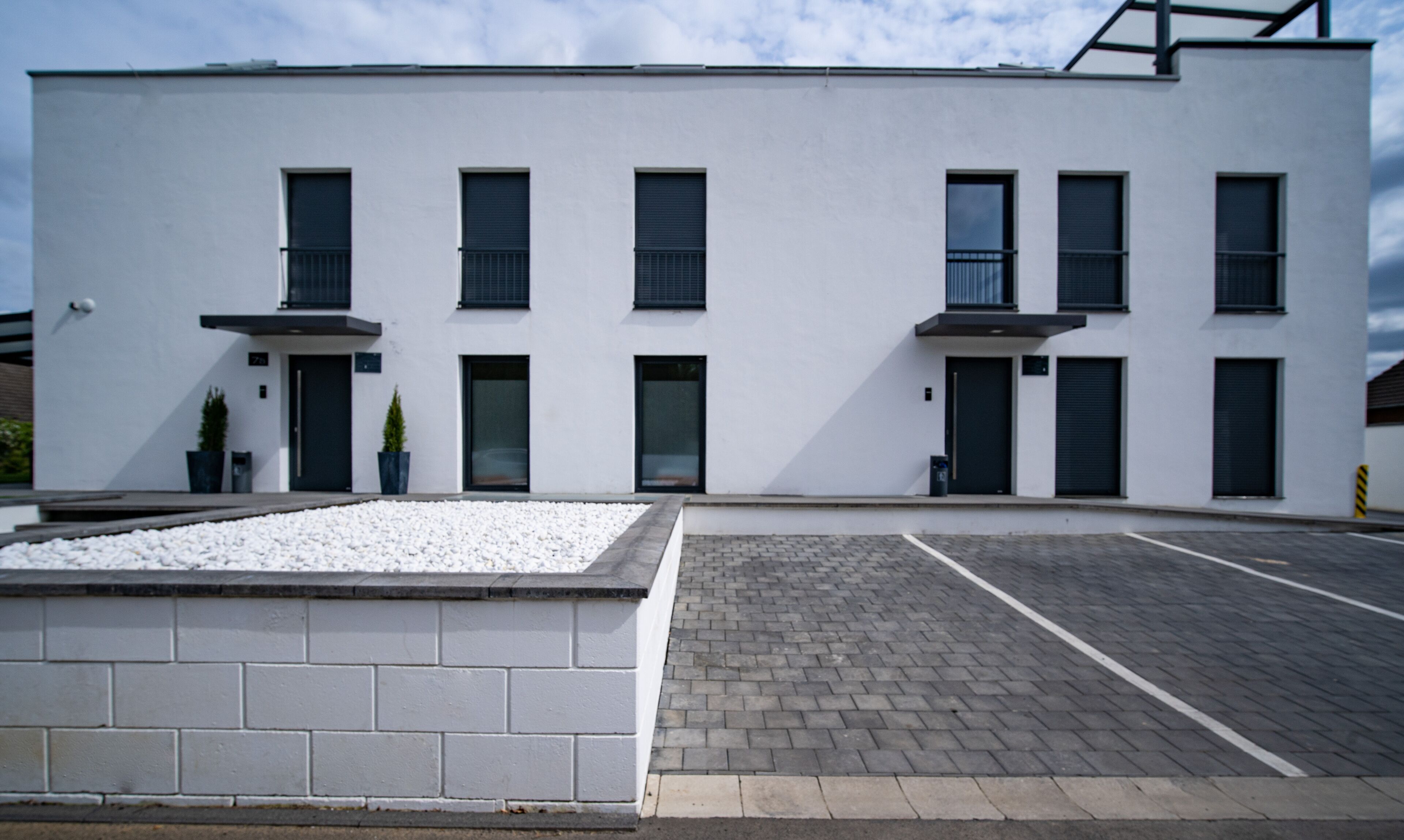 Un bâtiment moderne doté d’un toit plat, de nombreuses fenêtres et d’un espace de stationnement dallé.