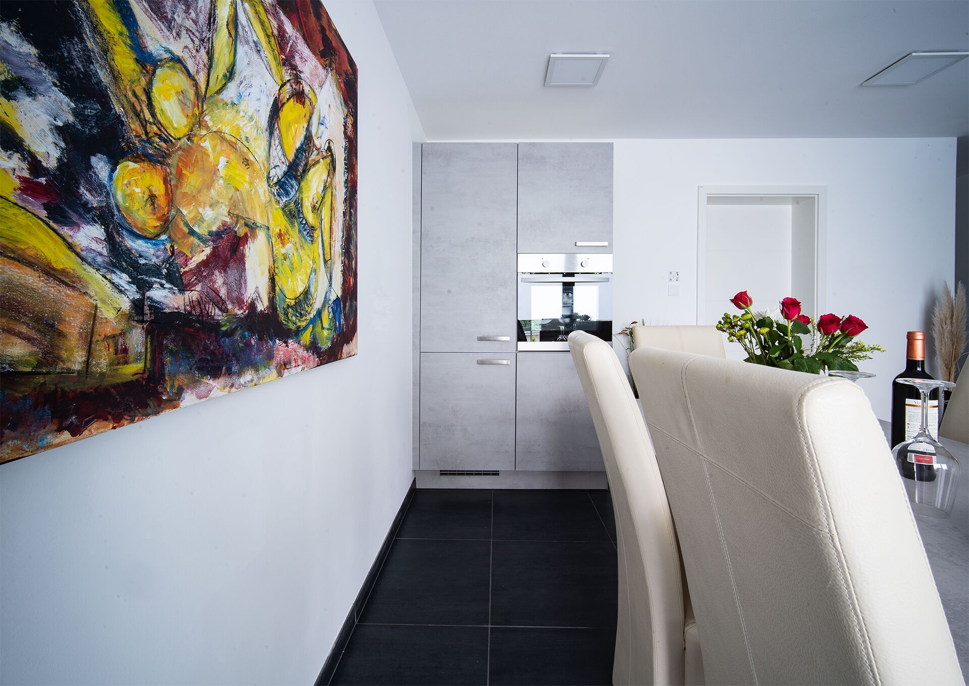 A modern kitchen with a built-in oven and a dining area with a chair and a vase of flowers.