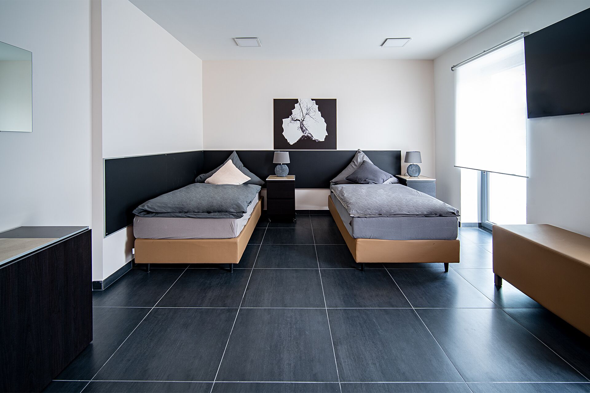Une chambre d’hôtel moderne équipée de deux lits simples, d’un bureau, d’une chaise, d’une télévision et d’une grande fenêtre.