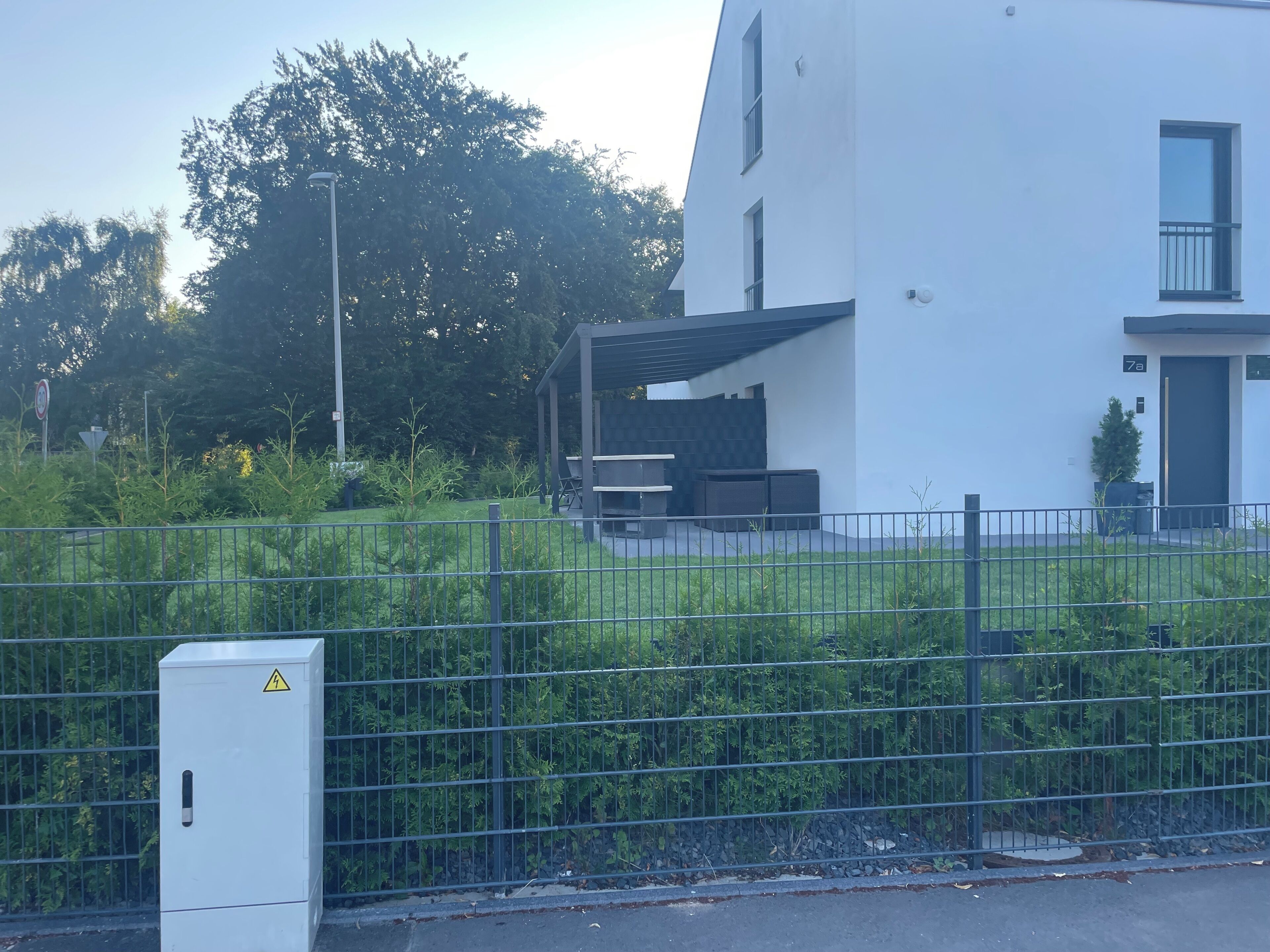 Ein modernes Gebäude mit flachem Dach, einem eingezäunten Garten und einem Technikschrank.