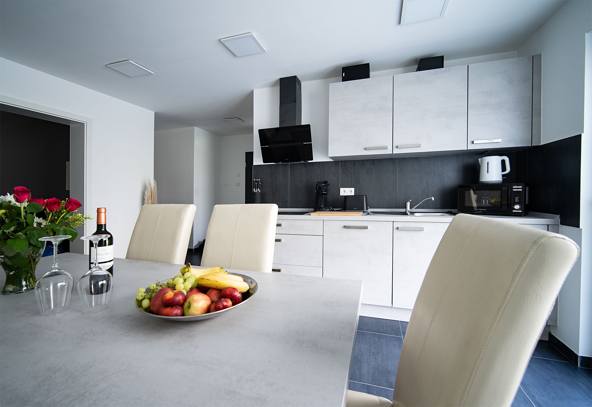 A modern kitchen with white cabinets, a dining table with chairs, and a fruit bowl.